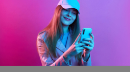 Portrait of young beautiful fashionable model wearing leather baker and baseball cap, holding smart phone in hands, texting with friends or checking social networks.